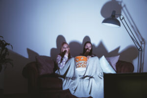 two girls watching a scary movie on the couch with popcorn.